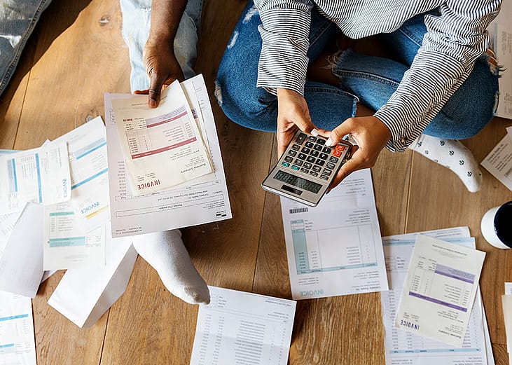 Two people on the floor managing debt by calculating invoices, bills and expenses.