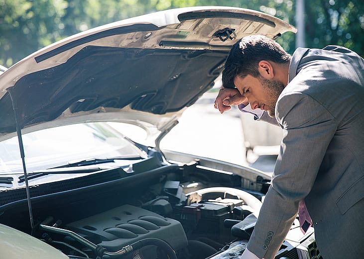 A car owner inspects his car's hood after it breaks down.