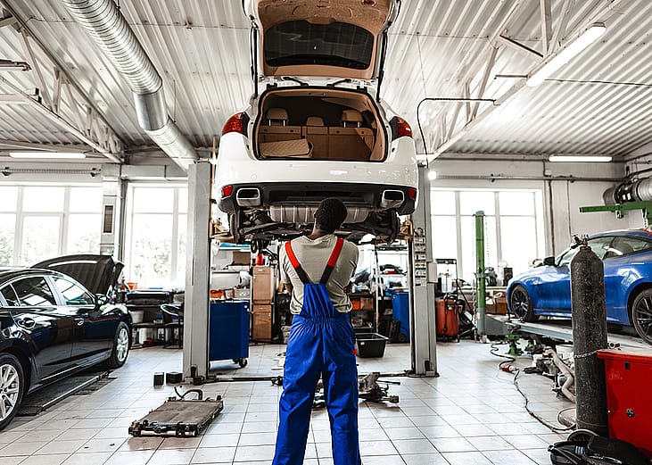 A pensive mechanic in a car service looking up a lifted car for repair.