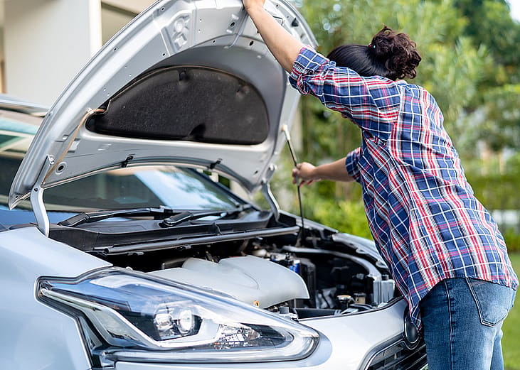 A female car owner opening the hood of her silver car to inspect its engine.