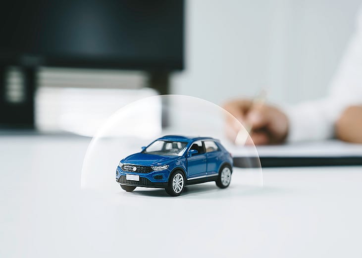 Miniature figure of a blue car with a shield illustration for insurance.