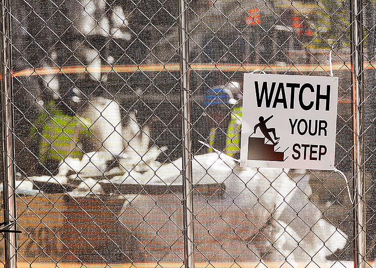 A 'watch your step' warning sign on the fence of a construction site.