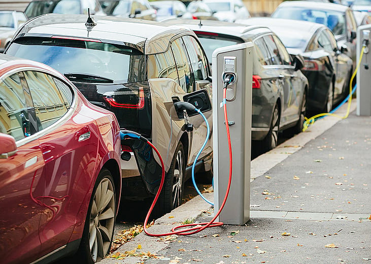 A lane of electric cars being charged on the side of a street.