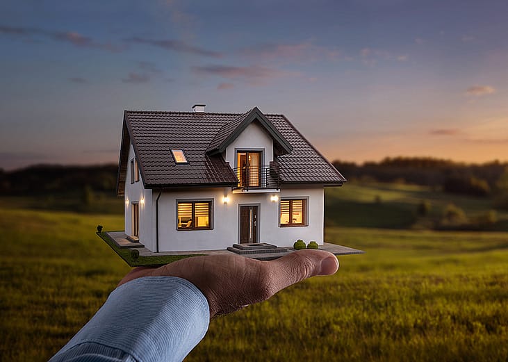 A figure of a house on a person's hand with a sunset background.