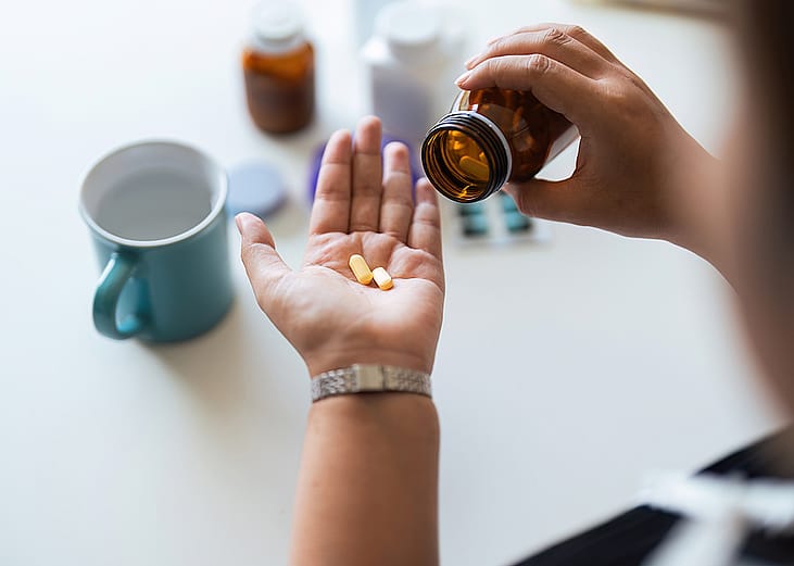 A woman's hand catching vitamin tablets from its bottle for daily intake.
