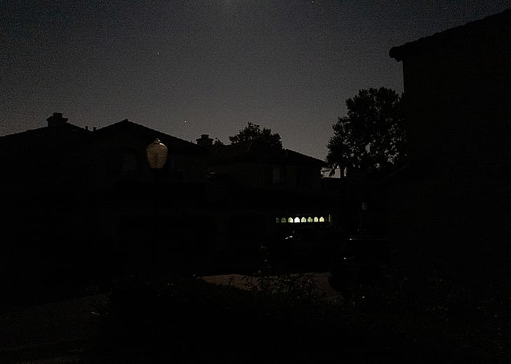 A suburban street in San Ramon, California is entirely dark except for a garage illuminated by a battery powered lantern during the Pacific Gas and Electric Public Safety Power Shutoff in 2019.