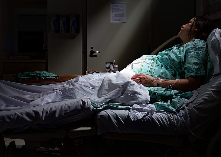 A pregnant woman in labor laying in a maternity ward bed with rays of sunlight on belly stomach.