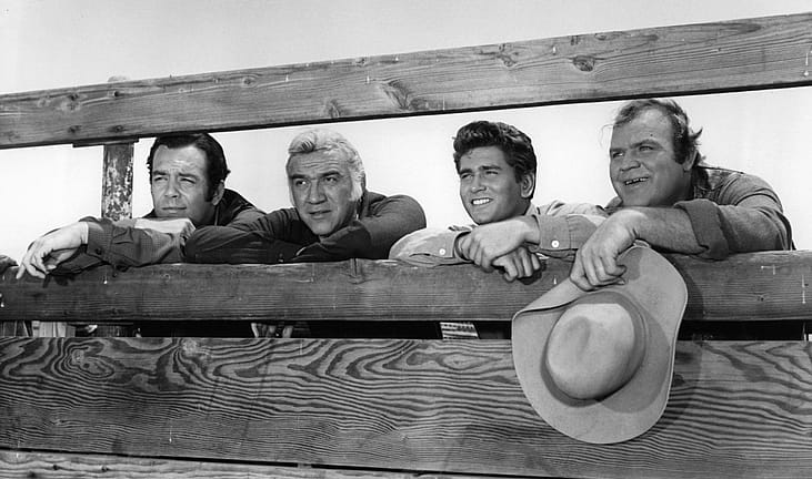 Dan Blocker holds his hat while standing with others in a scene from the TV series “Bonanza” (1959–1973).