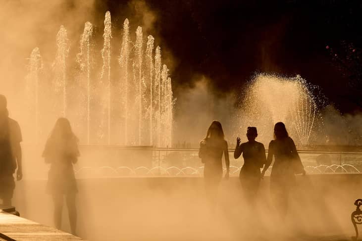 People walk through the fine spray of a fountain in the heat of the summer.