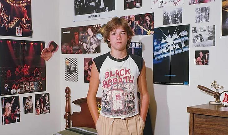 Teenager in a Black Sabbath shirt standing in his bedroom covered in Metal posters.