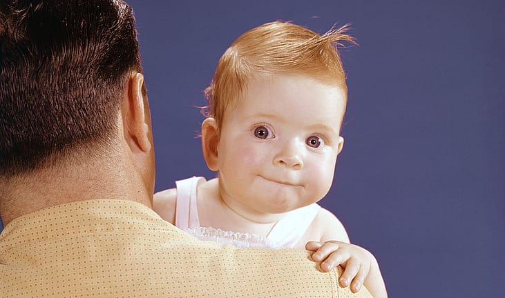 A red-haired baby looks over its father's shoulder.