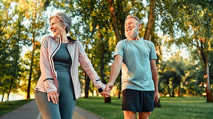 Modern active cheerful sports couple of senior people holding hands and talking cheerfully outdoors together.