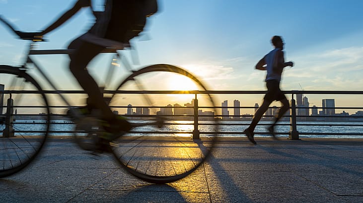 Silhouettes of jogger running and bicyclist cycling at sunset in front of the city skyline 