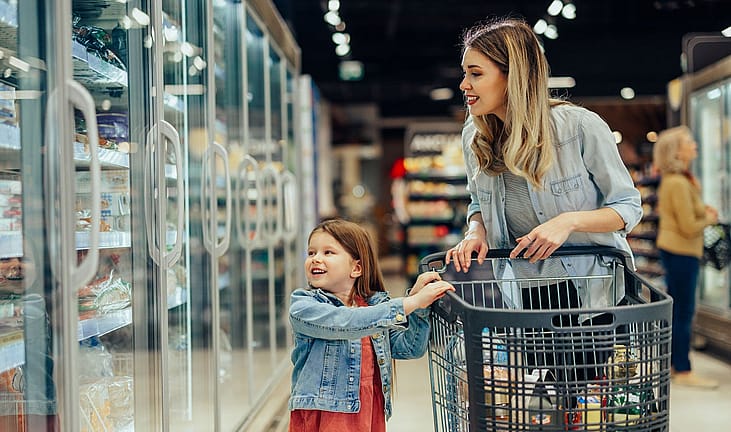 A mother and daughter in the frozen food aisle of a grocery store.