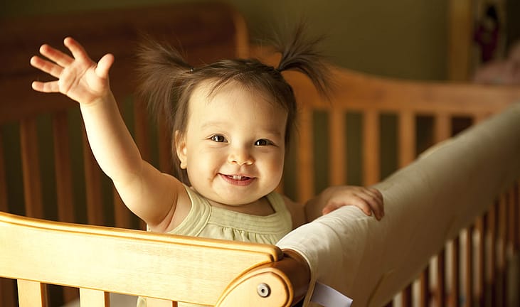 Baby girl in a crib waving