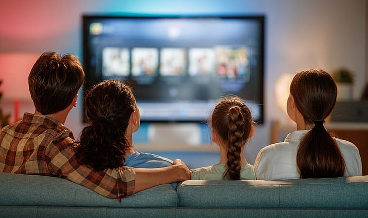 Family sitting on the couch watching television together. 