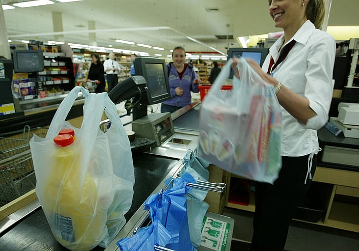 A smiling cashier at a grocery store bagging groeries.