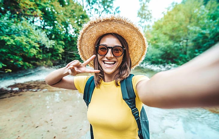 Happy female tourist with backpack taking selfie picture with smart mobile phone outside - Millenial woman having fun on adventure trip - Traveling and technology concept