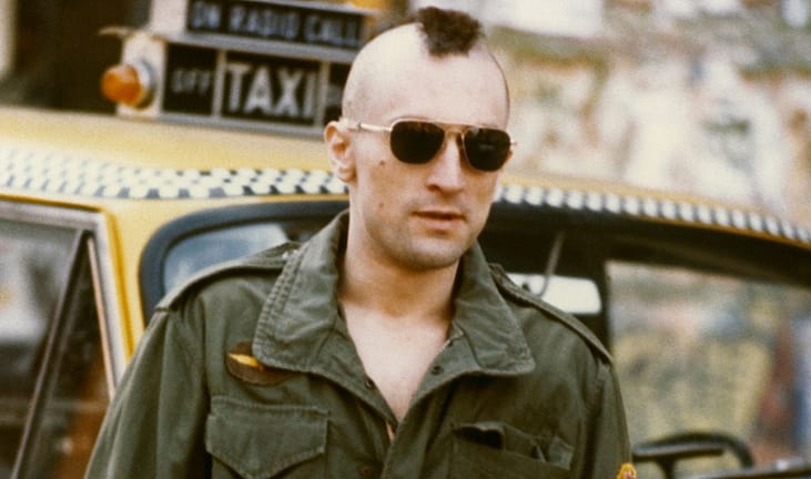 Robert De Niro, as Travis Bickle in the 1976 Martin Scorsese film 'Taxi Driver', with his iconic Mohawk haircut standing by a New York Yellow Taxi Cab.