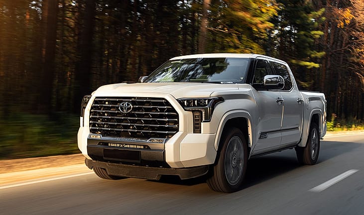 White Toyota Tundra pickup truck driving on a forest road at golden hour