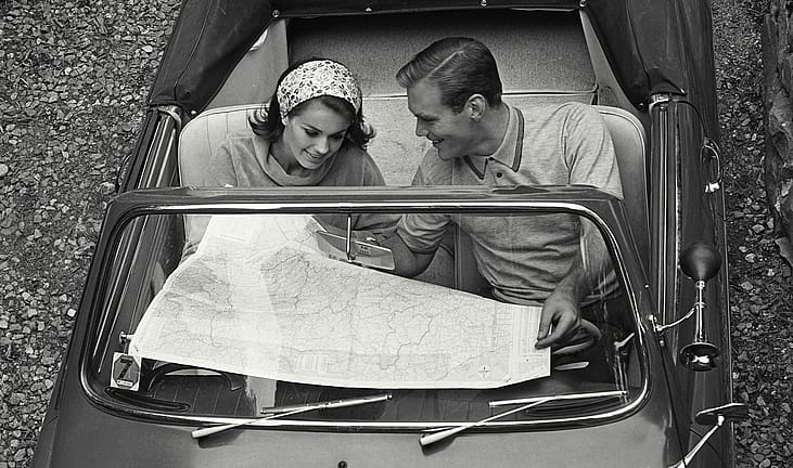 A black and white photo of a couple on reading a map on a road trip.