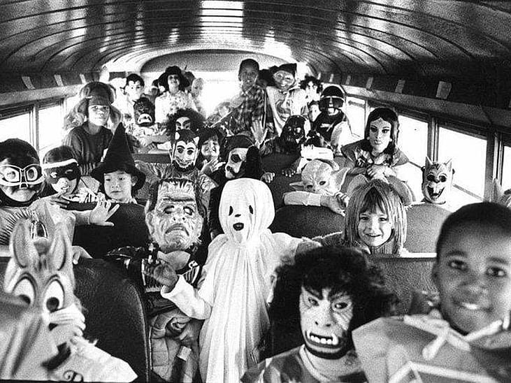 Black and white photo of a school bus filled with children all dressed up for Halloween in the 1980s
