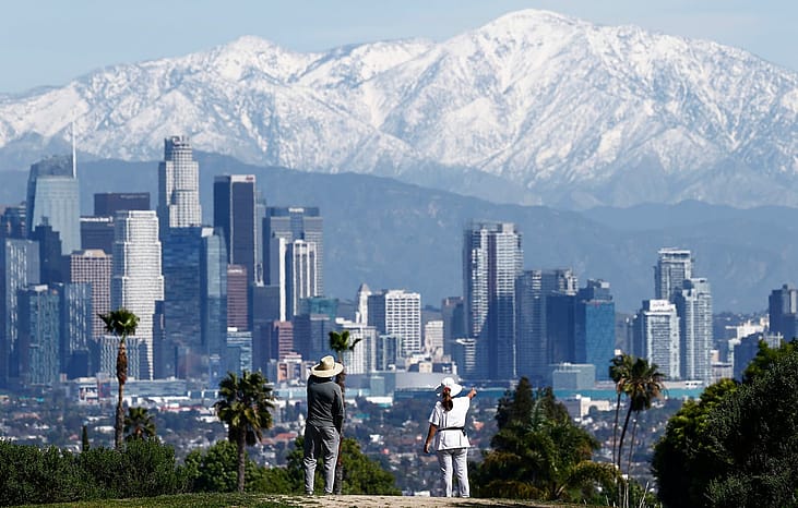 People take in the view of the downtown skyline with the snow-capped San Gabriel Mountains visible beyond on February 23, 2026 in Los Angeles, California.