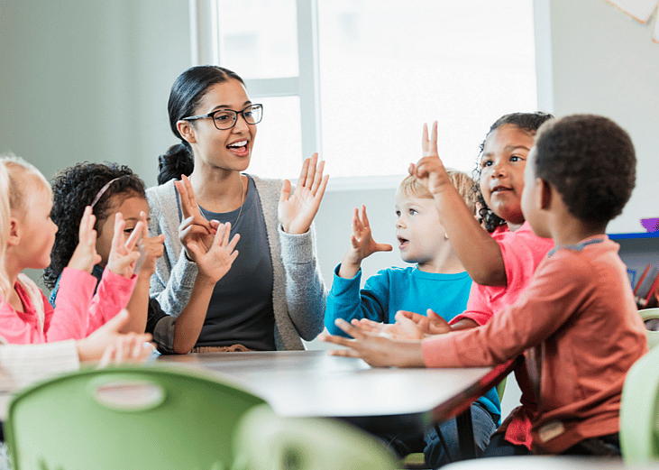 A young teacher sitting with her students at a table.