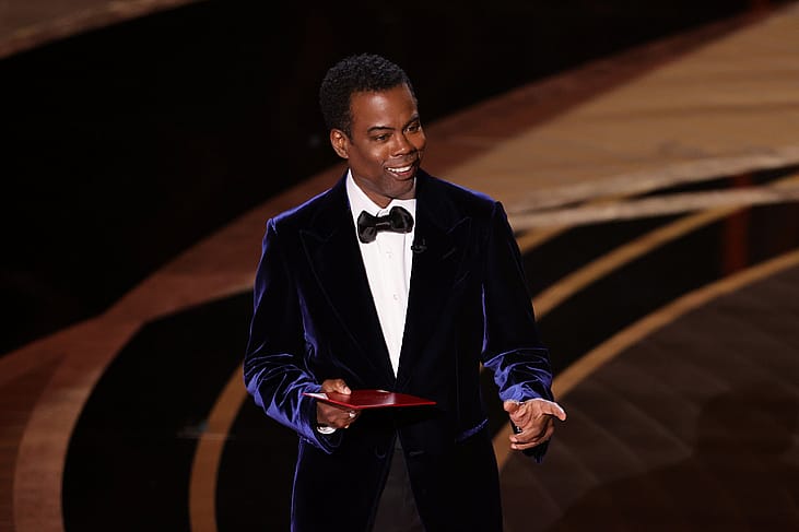 Chris Rock in a blue velvet suit on stage.