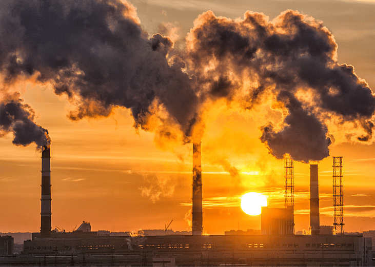 Dark gray smoke billows out of factory stacks as the sun sets. 
