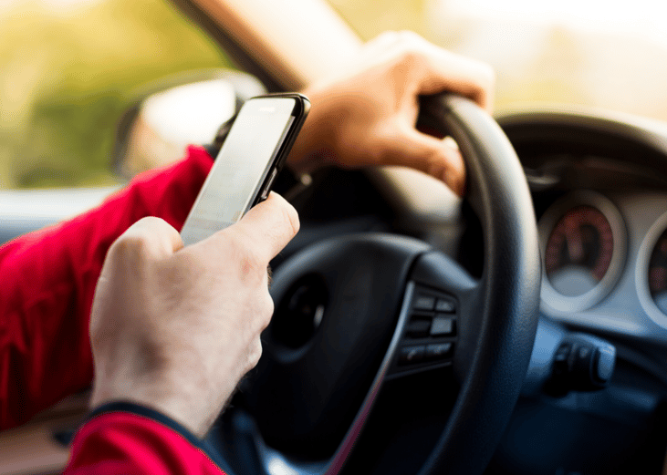 Driver with one hand on the steering wheel and one hand texting.