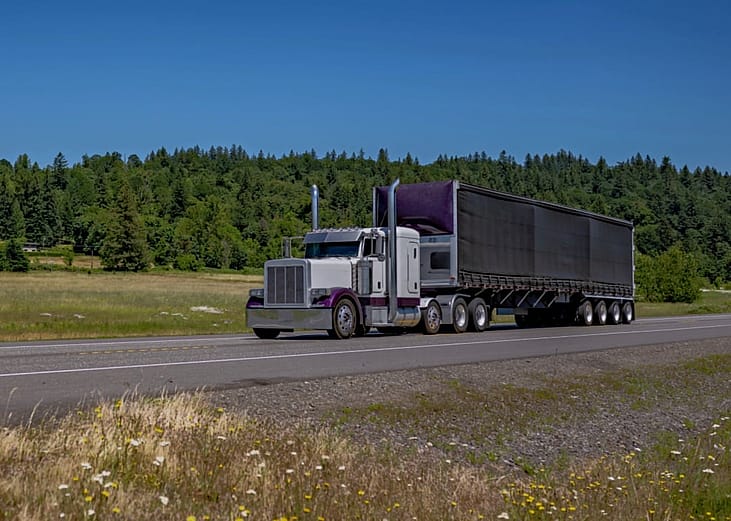 A large semi-truck driving along a highway in a rural area.