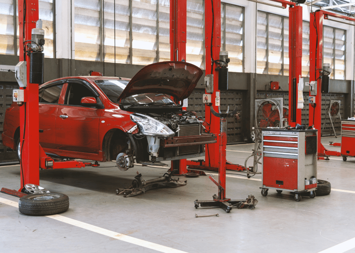 A damaged red car in an auto repair station.