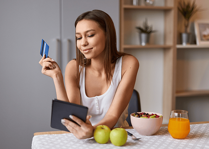 A happy woman shopping online during breakfast.