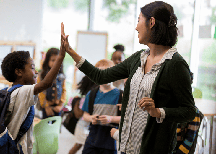 An elementary school teacher high-fiving a student.