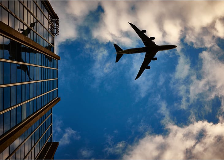 A silhouette of a airliner against blue skies, reflected in a tall building.