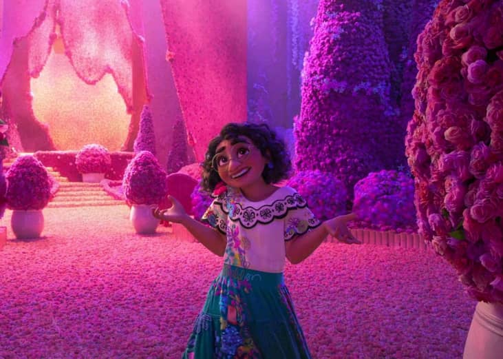 An animation of a woman smiling in a courtyard covered in pink and purple flowers.