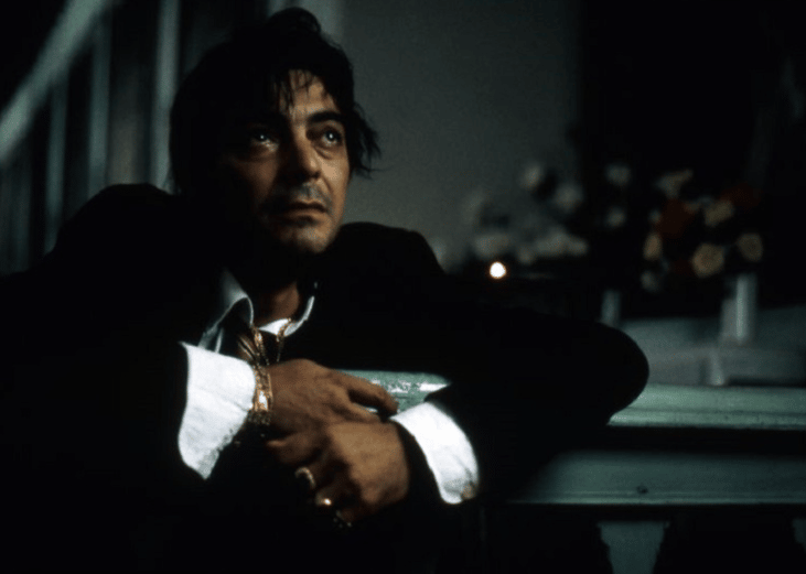 A disheveled man in a suit crouching down and looking up.