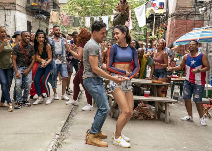 A young man and woman dancing on the street surrounded by a cheering crowd.