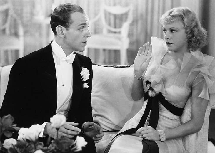 A man in a suit leaning in towards a woman in a gown with her hand up.