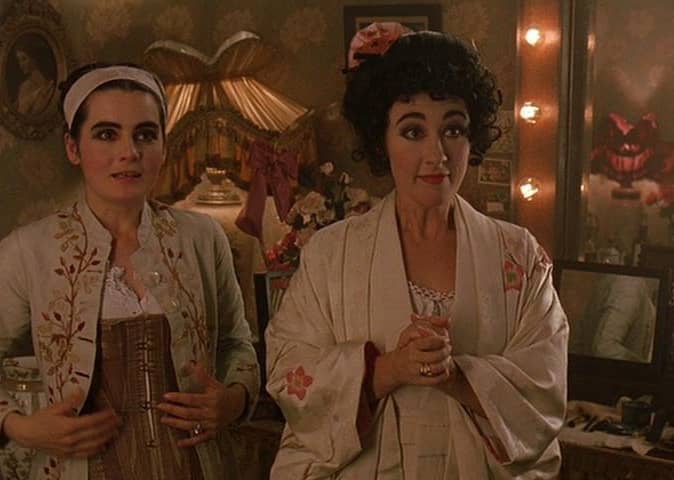 Two women in a historic dressing room with floral wallpaper. 