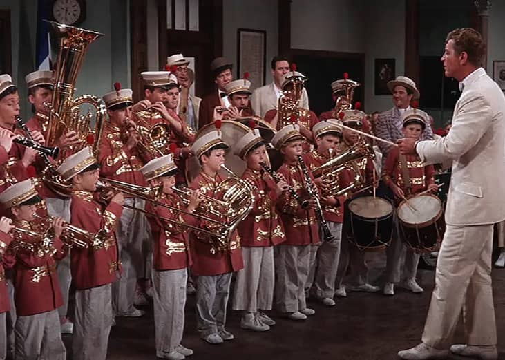 A man in a white suit leading a group of young kids playing instruments in uniform.