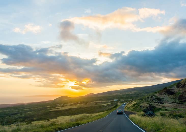 Cars driving down a road to a volcano at sunset in Maui, Hawaii.