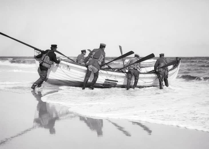 U.S. Coast Guard launching a wooden rescue boat on the beach.