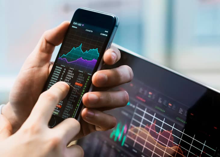 Business man holding phone with stock market displayed.
