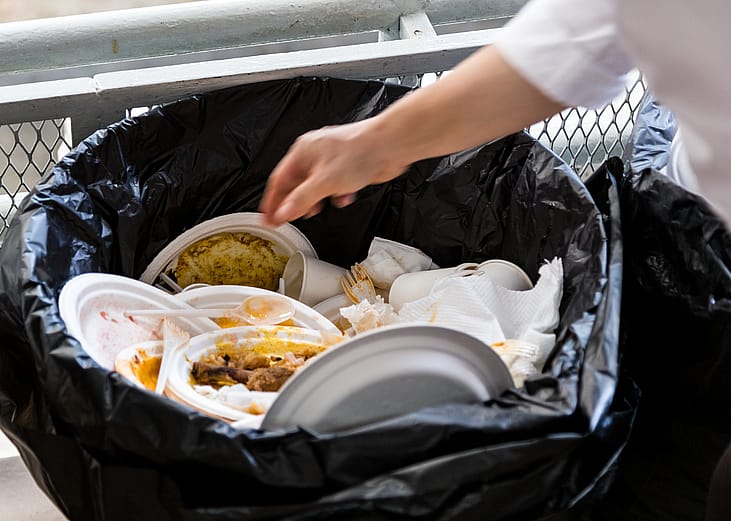 Hand throwing away styrofoam plates and cups in plastic bag.