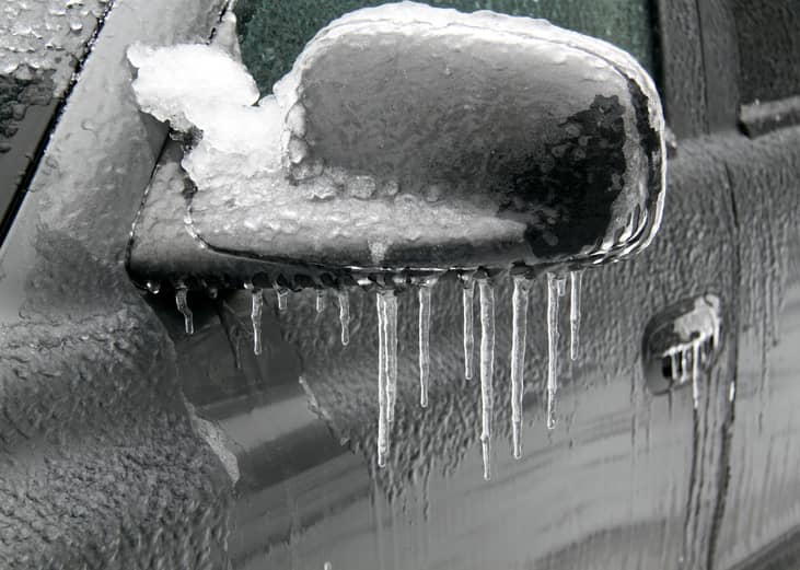A car side mirror covered in ice with icicles.