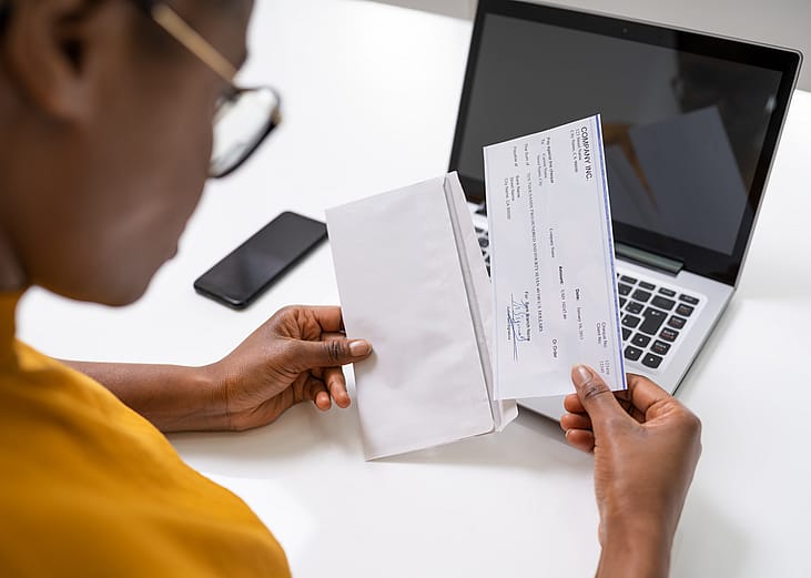 Woman holding and looking at a paycheck out of an envelope.