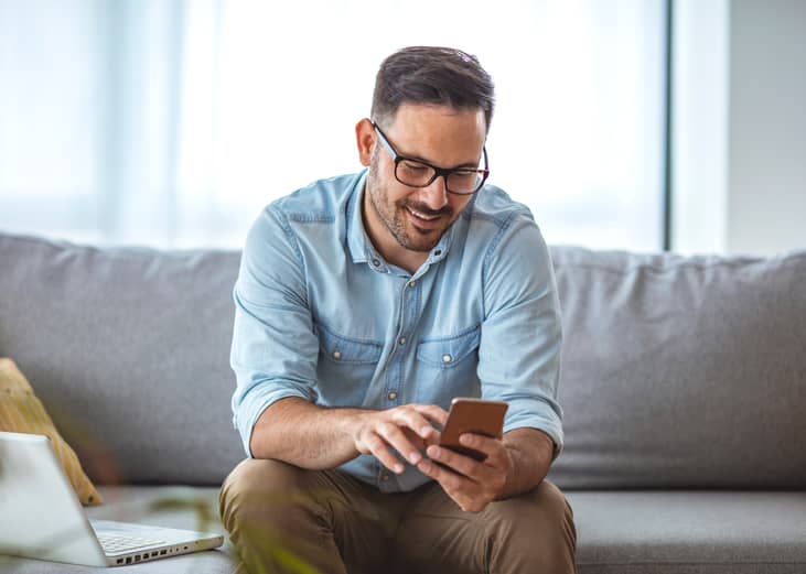 Man with spectacles sitting on couch while looking at mobile phone.