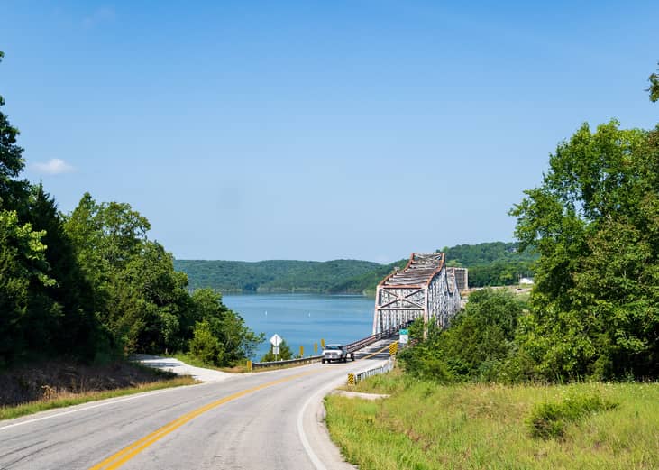 Asphalt road leading to bridge over lake.